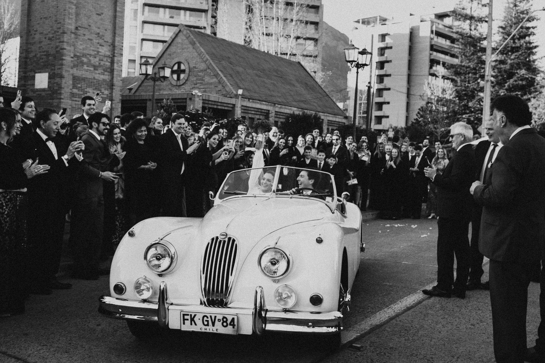 Newlyweds leaving the church in a classic open-top car as guests applaud