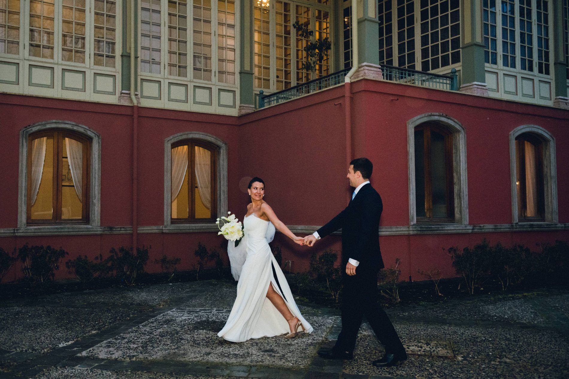 Couple walking hand in hand past a red villa at dusk