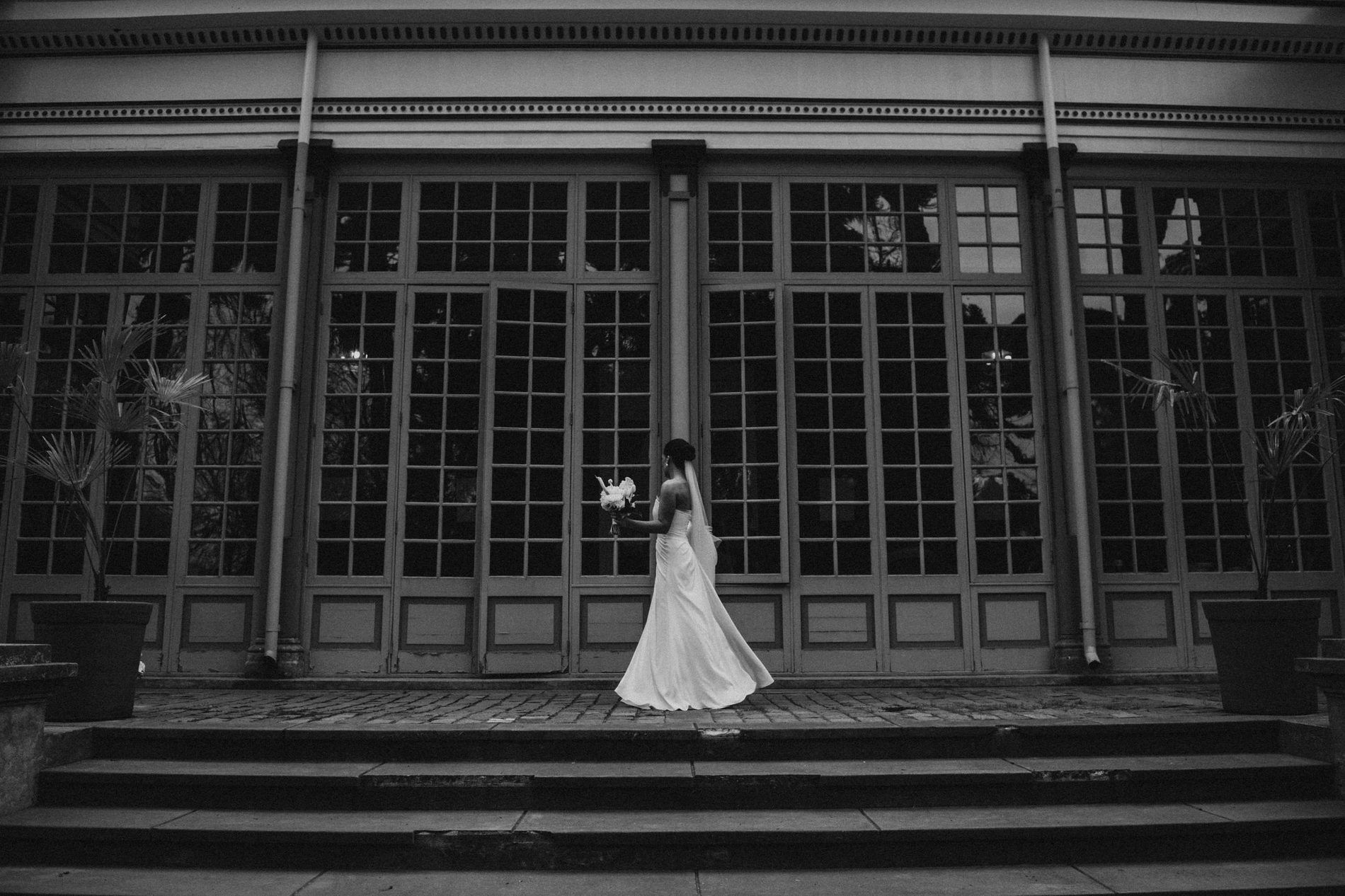 Bride walking past tall orangery windows with her bouquet